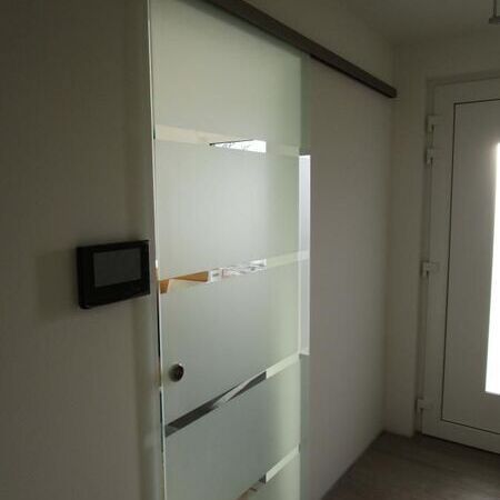Vor der Wand laufende Glasschiebetür mit sichtbarer Schiene, geschlossen