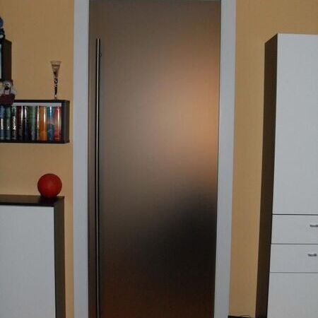 Raumhohe Glasschiebetür aus satiniertem Glas mit verdeckter Schiene, in die Wand laufend