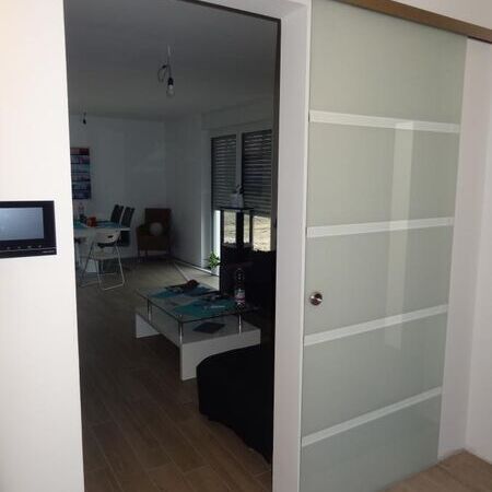 Vor der Wand laufende Glasschiebetür mit sichtbarer Schiene, offen stehend